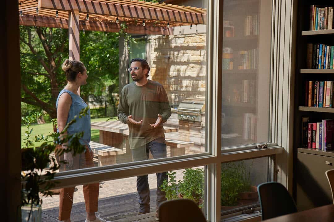 Aptive Pest Control Specialist Speaks With A Homeowner Outside On A Patio, Viewed Through A Window. Aptive Pest Control Specialist Speaks With A Homeowner Outside On A Patio, Viewed Through A Window.